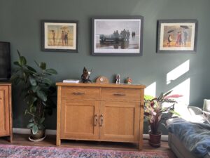 A green wall with a sideboard in front and pictures hanging on the wall.