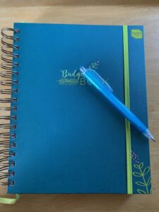 A blue budget book with a pen to help keep a spending diary.