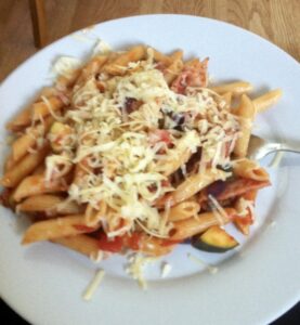 a plate of pasta with bacon and vegetables and grated cheese