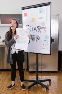 Woman in a grey coat holding white paper in front of a sign saying start up
