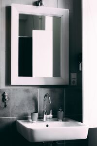 A mirror above a bathroom sink with grey tiling