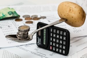 A spoon balancing over a calculator, with coins on one end and a potato on the other