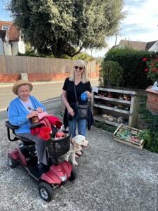 An elderly woman on a mobility scooter, a younger woman holding a dog