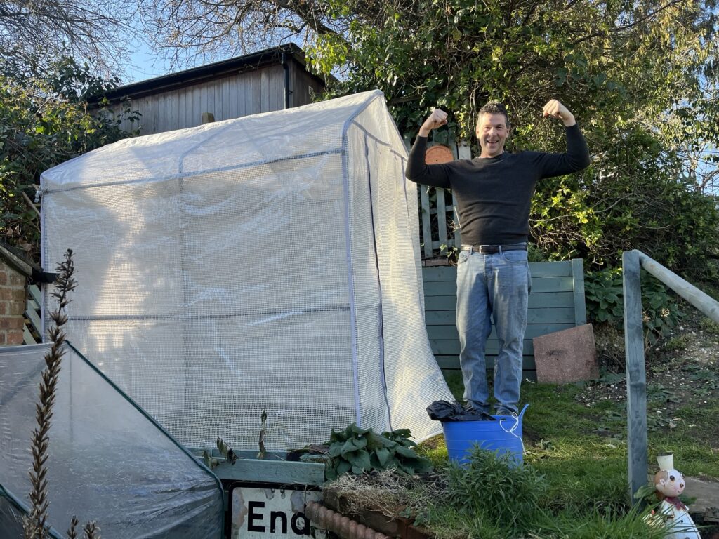 A man standing next to a plastic greenhouse showing his muscles