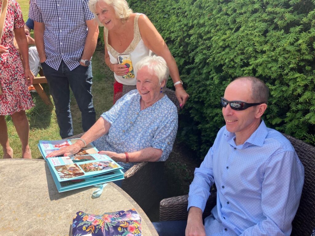 Some people sitting outside at a table looking at a book of photos